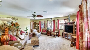 Un salon comprenant un canapé, des fauteuils, un téléviseur, un ventilateur de plafond et un vase décoratif.