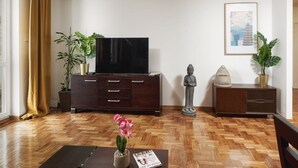 A living room with a flat-screen TV on a wooden cabinet, a Buddha statue, a framed picture on the wall, and two potted plants. - Warsaw Home Near Center (Warsaw)