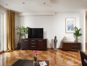 Ein Wohnzimmer mit Flachbildfernseher auf einer Holzkassette, einer Buddha-Statue, einem gerahmten Bild an der Wand und zwei Blumentöpfen.