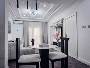 A modern living room with a round dining table, two chairs, a sofa, a TV, and a decorative ceiling light. - Luxury Penthouse in Lekki 1 with Fast Wi-Fi & 24/7 Power (Lagos)