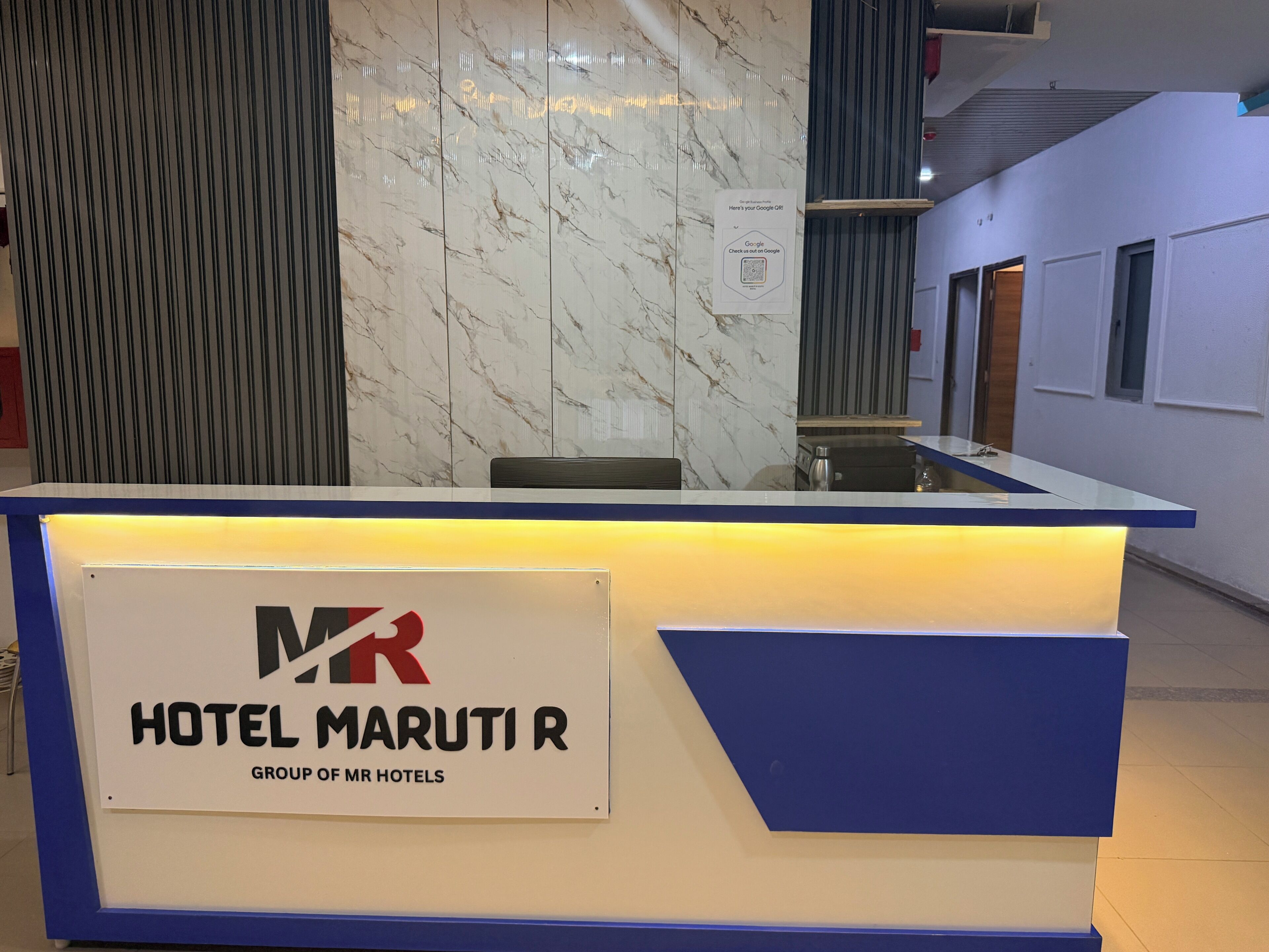 Uma receção de hotel com parede de mármore e uma placa a indicar 'HOTEL MARUTI R GROUP OF MR HOTELS'.