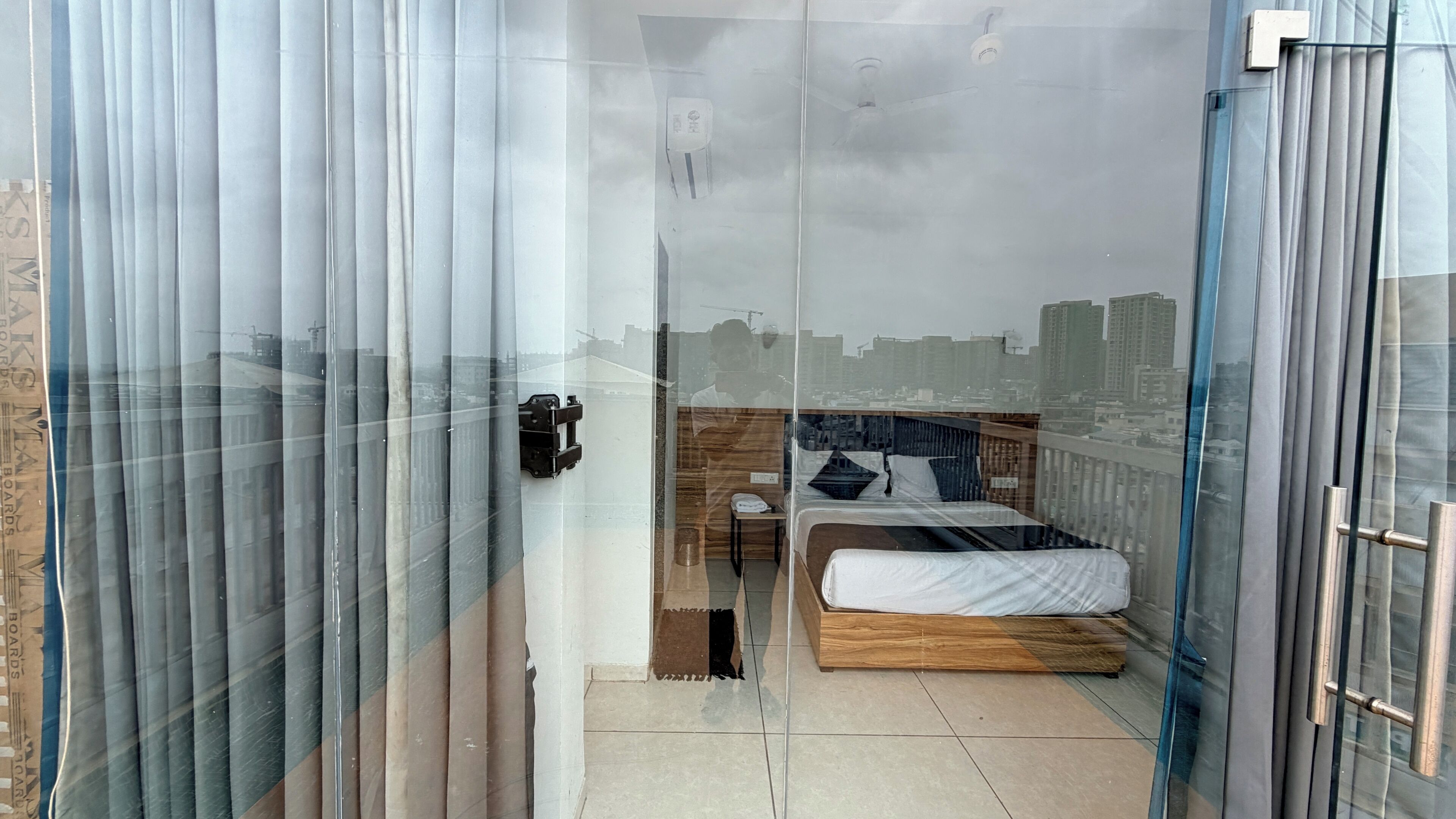 A modern bedroom with a bed, a nightstand, and a view of the city through a glass door.