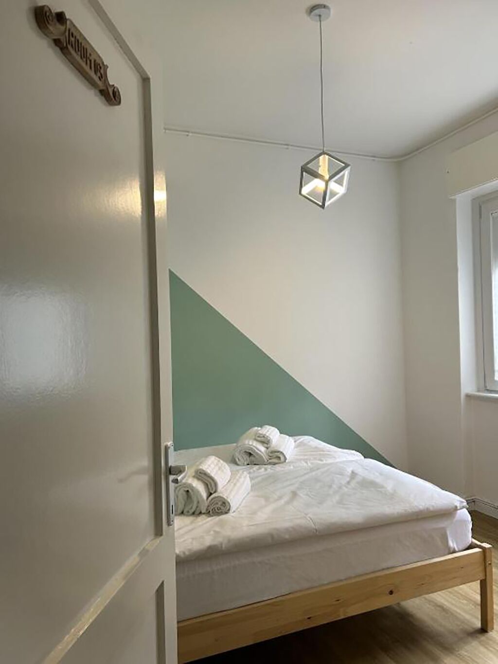 En enkeltseng med træramme, en hængende lampe og en dør med et skilt.