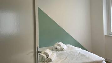 Un letto singolo con struttura in legno, una lampada a sospensione e una porta con un cartello.