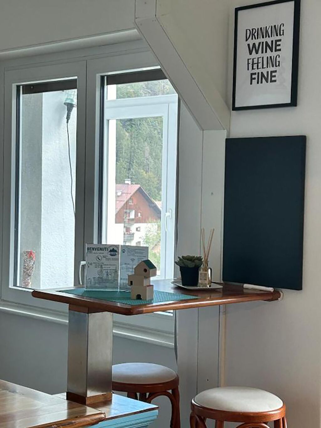 Ein Zimmer mit Schreibtisch, zwei Stühlen, einem gerahmten Schild an der Wand und einem Fenster mit Blick auf Gebäude.