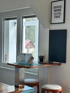 Una habitación con un escritorio, dos sillas, un cartel enmarcado en la pared y una ventana con vistas a edificios.
