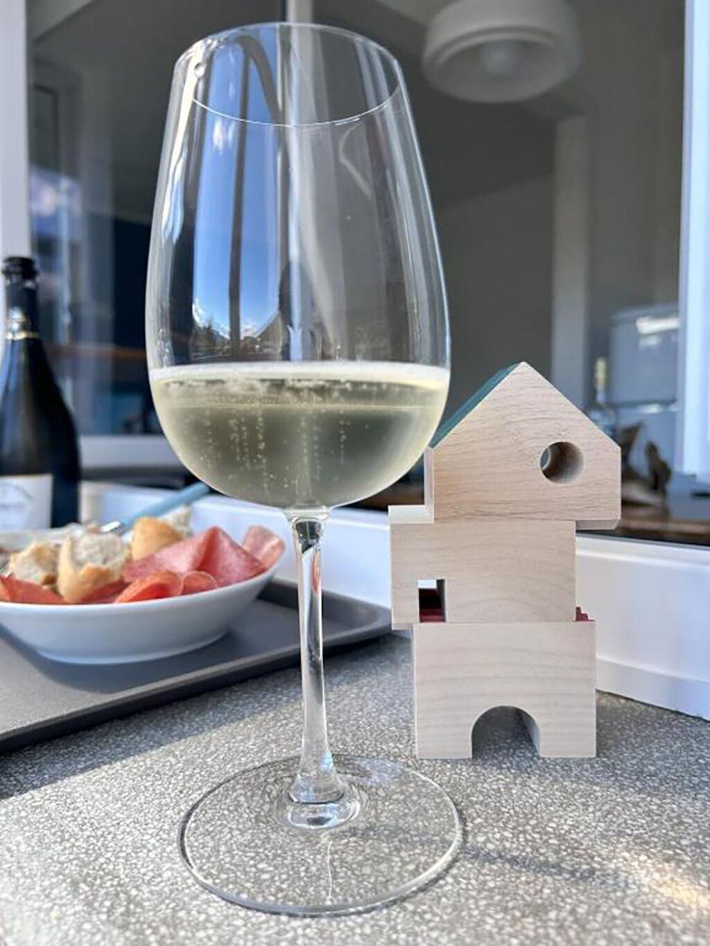 Een wijnglas met een onderzetter in de vorm van een huisje op een aanrecht.