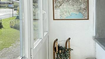 Un couloir avec une fenêtre, une carte encadrée, un présentoir à plantes en bois et une poubelle.