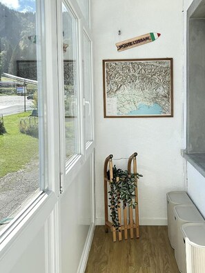 A hallway with a window, a framed map, a wooden plant stand, and a trash bin.