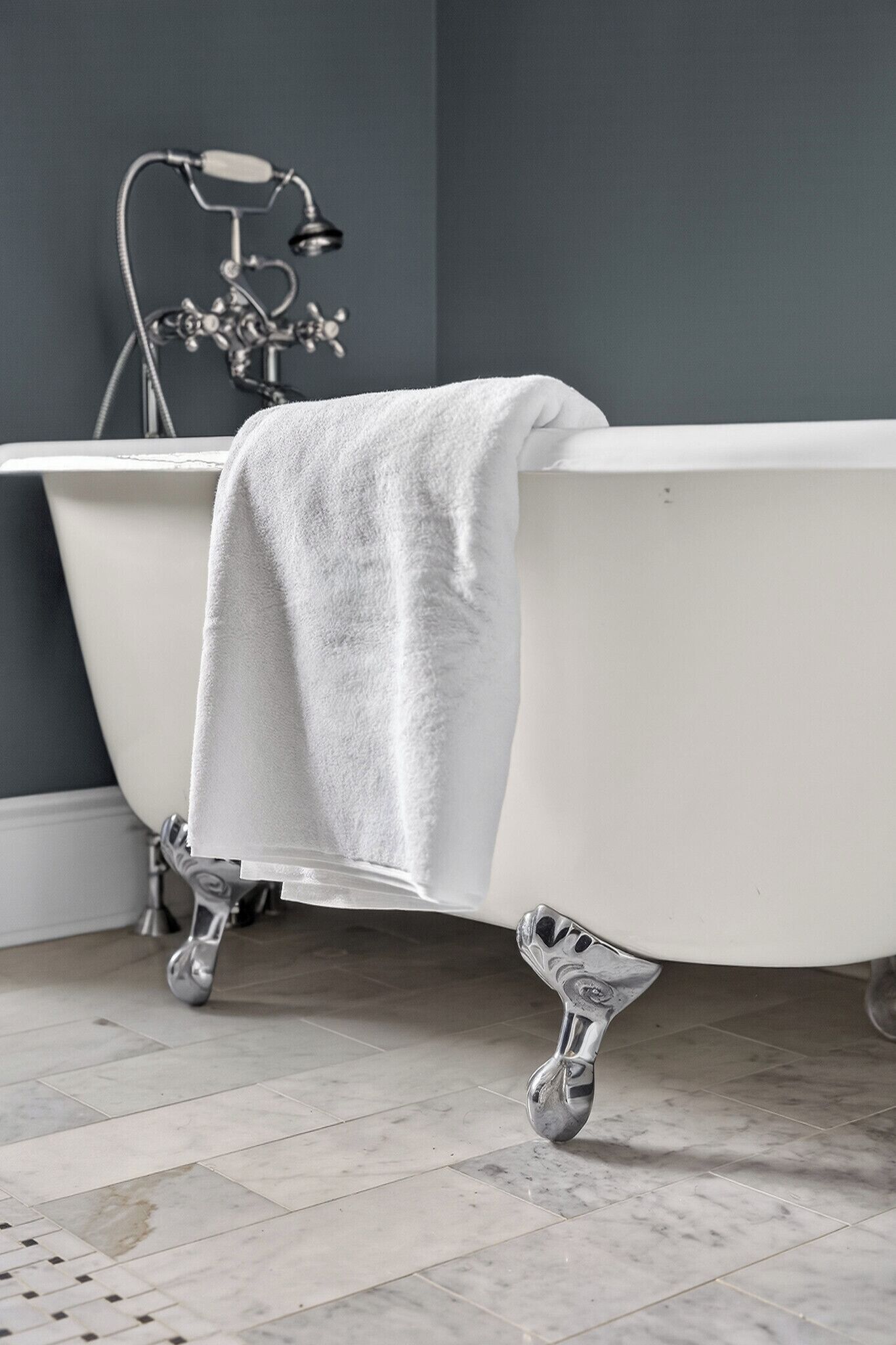 A bathroom with a white clawfoot bathtub, a vintage faucet, and a tiled floor.