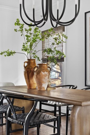 Un coin repas avec une table en bois, deux vases en céramique ornés de plantes, des chaises noires et un luminaire moderne.