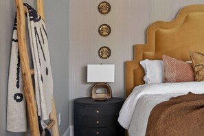 Een slaapkamer met een bed, nachtkastje, lamp en een wand met decoratieve borden.