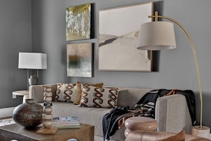 Ein modernes Wohnzimmer mit einem grauen Sofa, dekorativen Kissen, einem runden Couchtisch mit Büchern und einer Stehlampe.