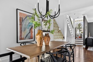 A dining area with a wooden table, two large vases, black chairs, and a chandelier with greenery. - Uptown Charlotte Luxury 4 bedroom Townhouse walkable to everything (Charlotte)