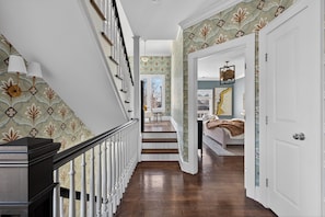 Eine Treppe mit gemustertem Wandpapier, ein Holzboden und ein Bett mit Decke in einem Schlafzimmer.