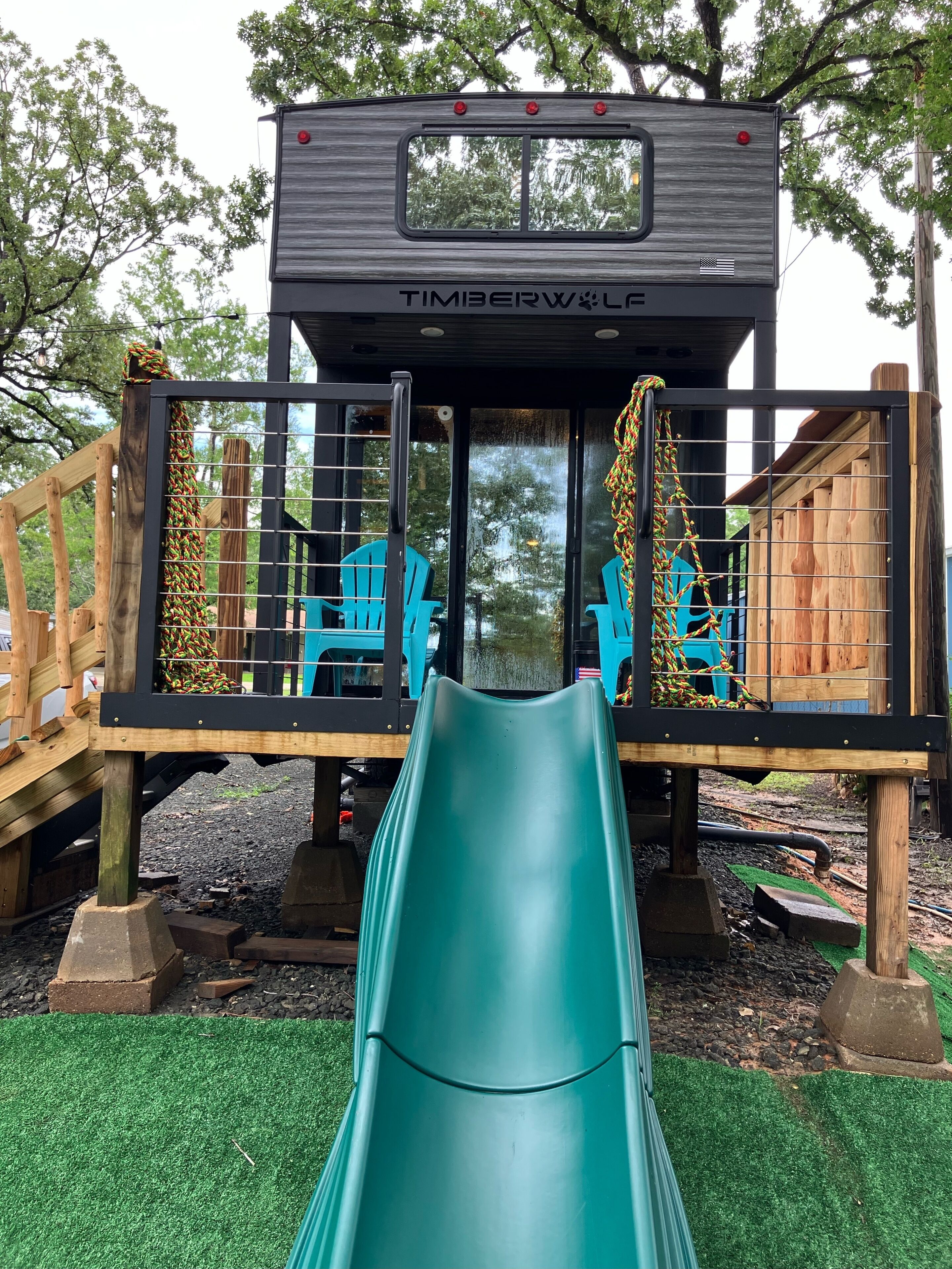 A playground with a slide, a play structure, and a deck with chairs.