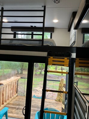 Ein Zimmer mit Etagenbetten, einem Fenster mit Blick auf eine Terrasse und einen Außenbereich sowie einem Deckenventilator.