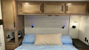 A bedroom with a bed, wooden cabinets, a wall-mounted fan, and two wall sconces. - Beautiful 3-bedroom recreational vehicle with water view in Bronson (Bronson)