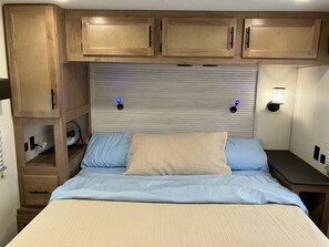 A bedroom with a bed, wooden cabinets, a wall-mounted fan, and two wall sconces. - Beautiful 3-bedroom recreational vehicle with water view in Bronson (Bronson)
