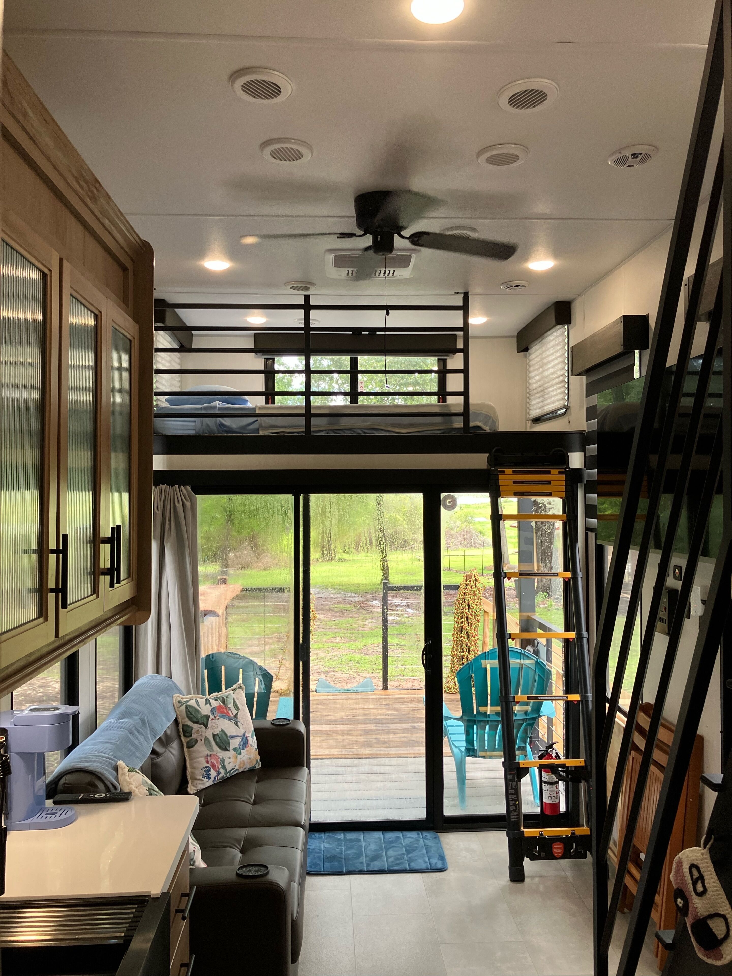 A modern interior with a bunk bed, a sofa, a dining table, and a view of a green outdoor area.