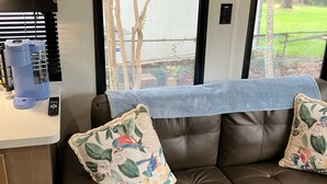 A brown leather sofa with floral cushions, a coffee maker, and a remote control on a counter. - Beautiful 3-bedroom recreational vehicle with water view in Bronson (Bronson)