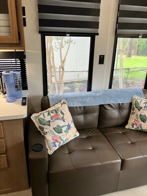 A brown leather sofa with floral cushions, a coffee maker, and a remote control on a counter. - Beautiful 3-bedroom recreational vehicle with water view in Bronson (Bronson)