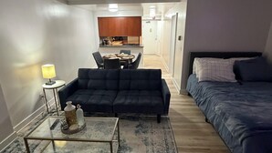 Um espaço compacto com sofá, cama, mesa de centro e área de refeições com cadeiras.