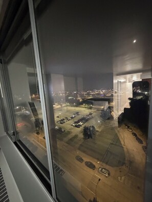 Blick aus einem Fenster bei Nacht auf einen Parkplatz mit mehreren Autos und einer entfernten Skyline.