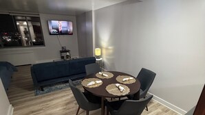 Uma sala de jantar com uma mesa redonda, quatro cadeiras e uma televisão fixada na parede.