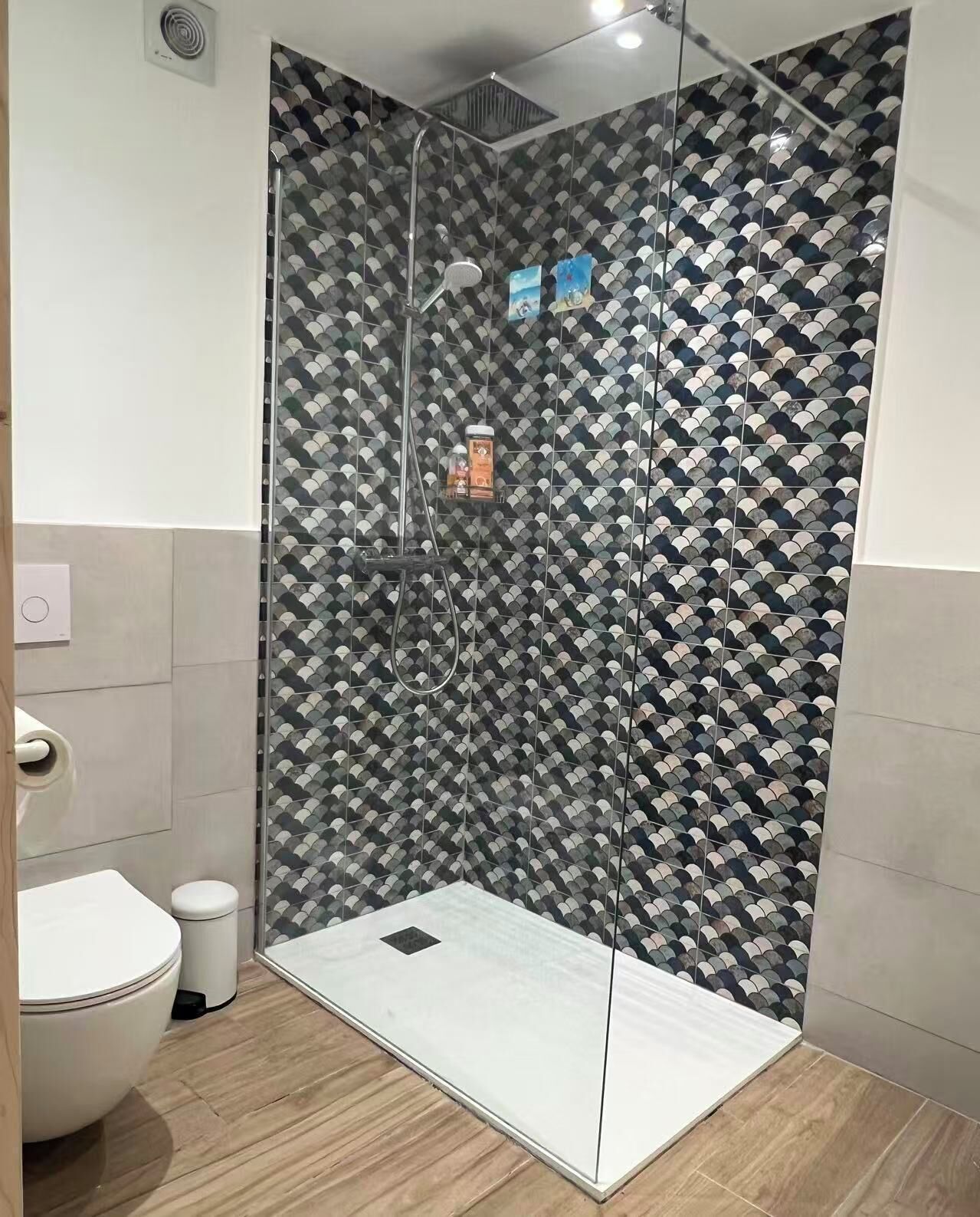 Een moderne badkamer met douchecabine, toilet en prullenbak.