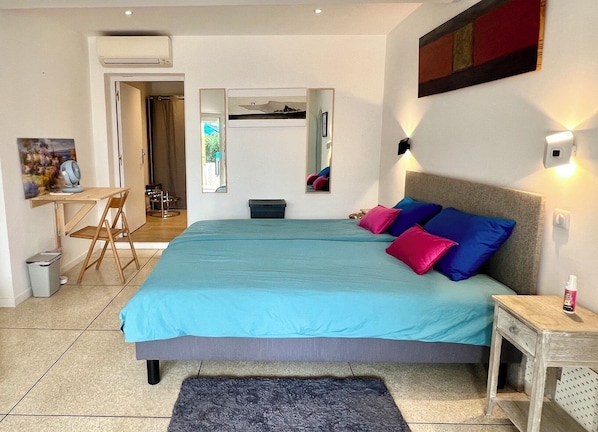 Un dormitorio con cama, almohadas, escritorio, silla y una mesita.
