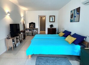 A bedroom with a bed, a television, a bookshelf, and a door leading to another room. - Guesthouse with a pool, 200 meters from the beach, air-conditioned (Roquebrune-sur-Argens)