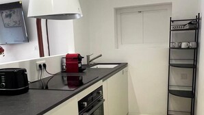 A compact kitchen with a black countertop, a red coffee maker, a white wall-mounted lamp, and a black metal shelf with cups. - Guesthouse with a pool, 200 meters from the beach, air-conditioned (Roquebrune-sur-Argens)