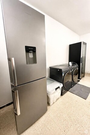 A compact kitchen area with a stainless steel refrigerator, a water dispenser, a washing machine, and a black refrigerator. - Guesthouse with a pool, 200 meters from the beach, air-conditioned (Roquebrune-sur-Argens)