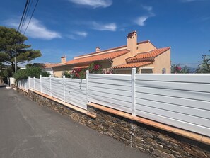 A house with a red-tiled roof, white fence, and stone foundation. - Guesthouse with a pool, 200 meters from the beach, air-conditioned (Roquebrune-sur-Argens)