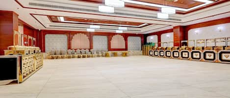 A spacious hall with a high ceiling, chandeliers, and a row of chairs along the walls.