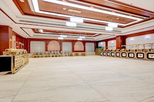 A spacious hall with a high ceiling, chandeliers, and a row of chairs along the walls.
