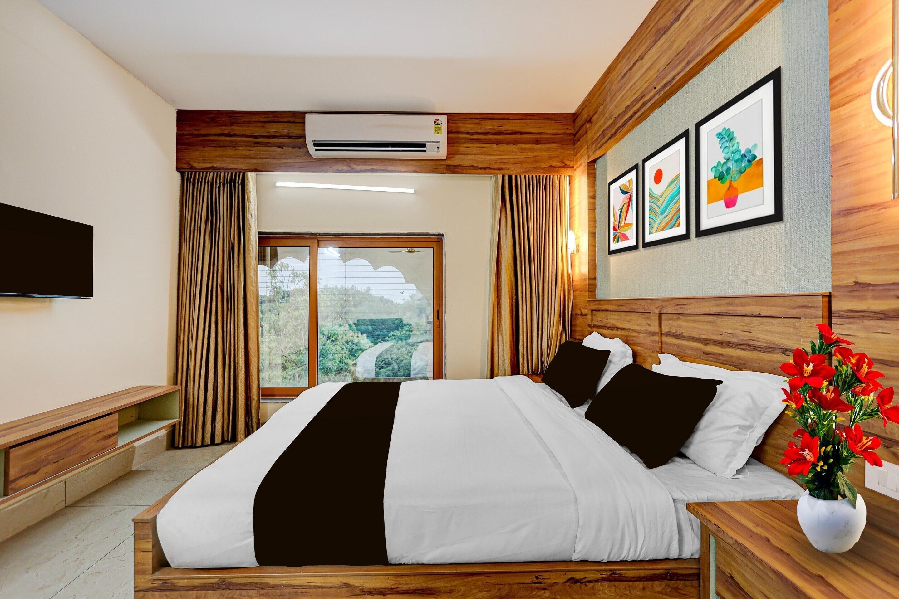 A hotel room with a bed, a flat-screen TV, a window with curtains, and artwork on the wall.