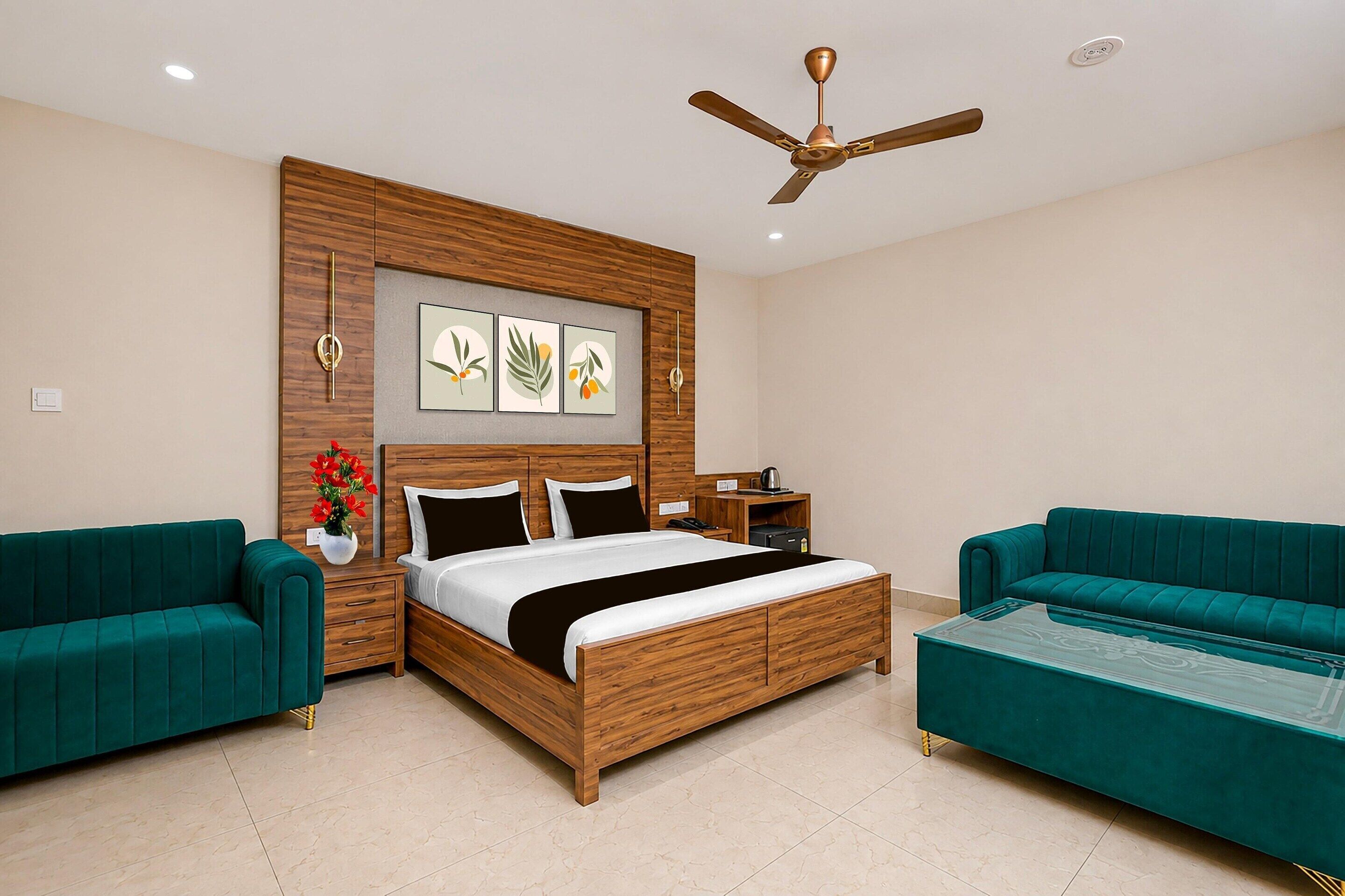 A modern bedroom with a wooden bed, two green sofas, a ceiling fan, and wall-mounted artwork.