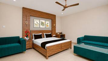 A modern bedroom with a wooden bed, two green sofas, a ceiling fan, and wall-mounted artwork.