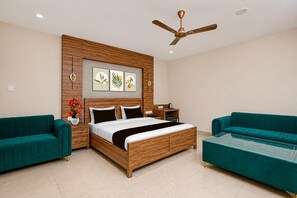 A modern bedroom with a wooden bed, two green sofas, a ceiling fan, and wall-mounted artwork.
