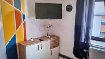 Una habitación con televisión de pantalla plana en la pared, un mueble de madera con cajones y un radiador.