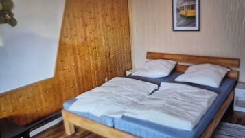 A single bed with a wooden headboard and a blue mattress cover in a room with wooden flooring and a wooden panel wall.