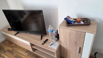 A wooden TV stand with a flat-screen TV, remote controls, a bottle of water, a glass, and a tray with snacks and a card.