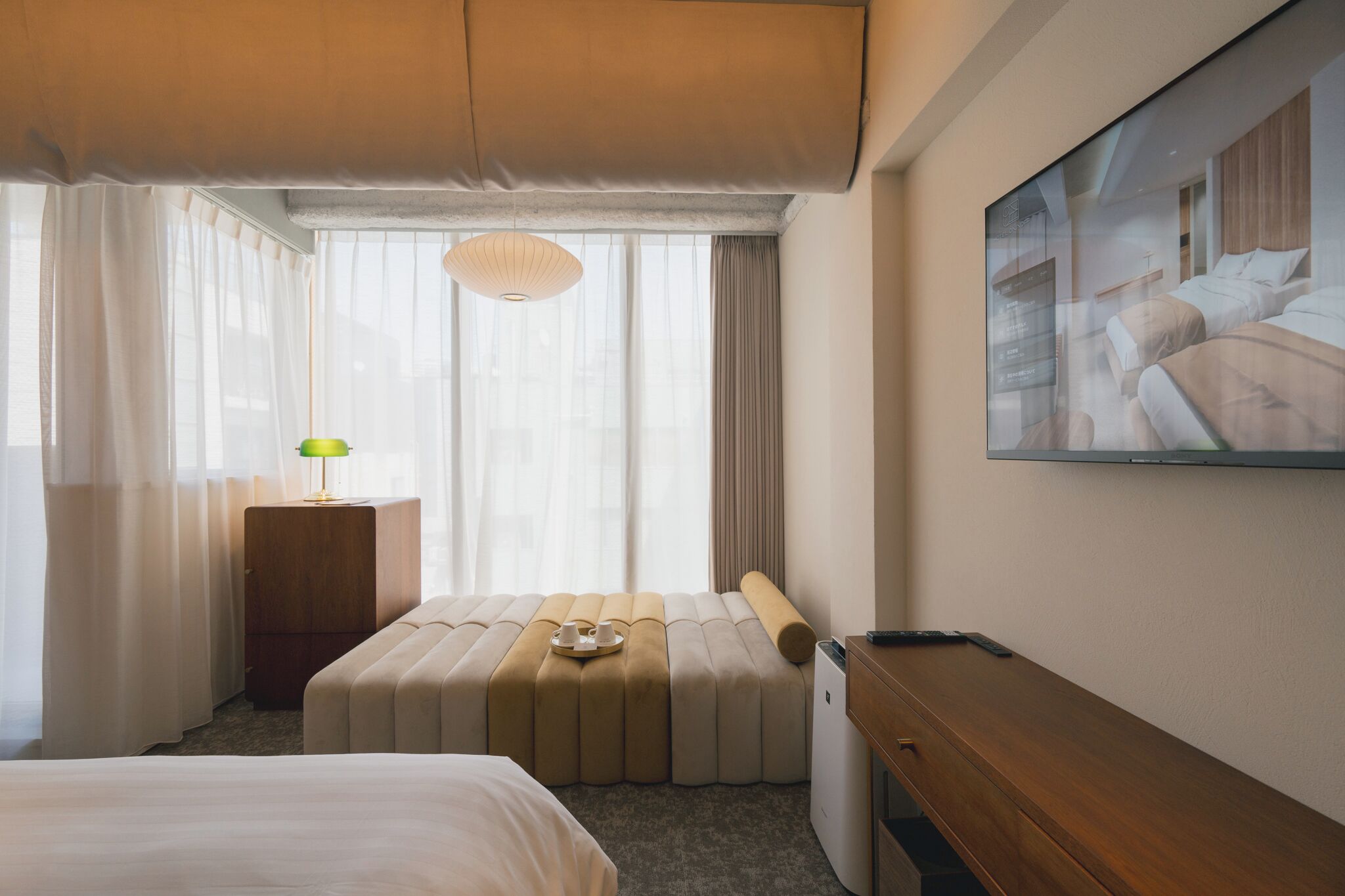 A hotel room with a bed, a desk, a chair, a lamp, and a painting on the wall.