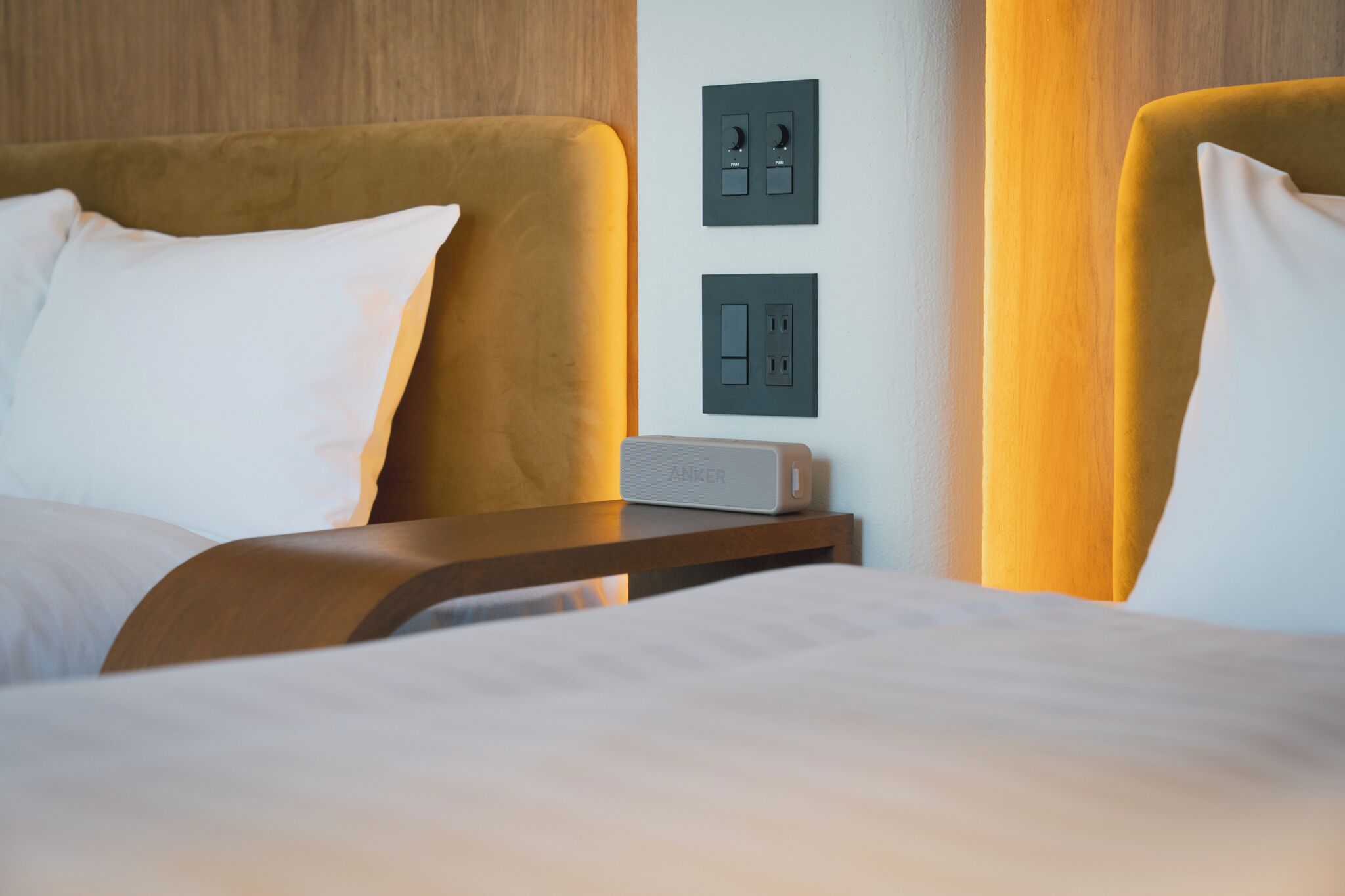A hotel room with a bed, bedside table, and wall-mounted power outlets.