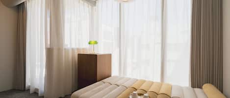 Una habitación de hotel con una cama grande, una mesita de noche con lámpara y cortinas traslúcidas.