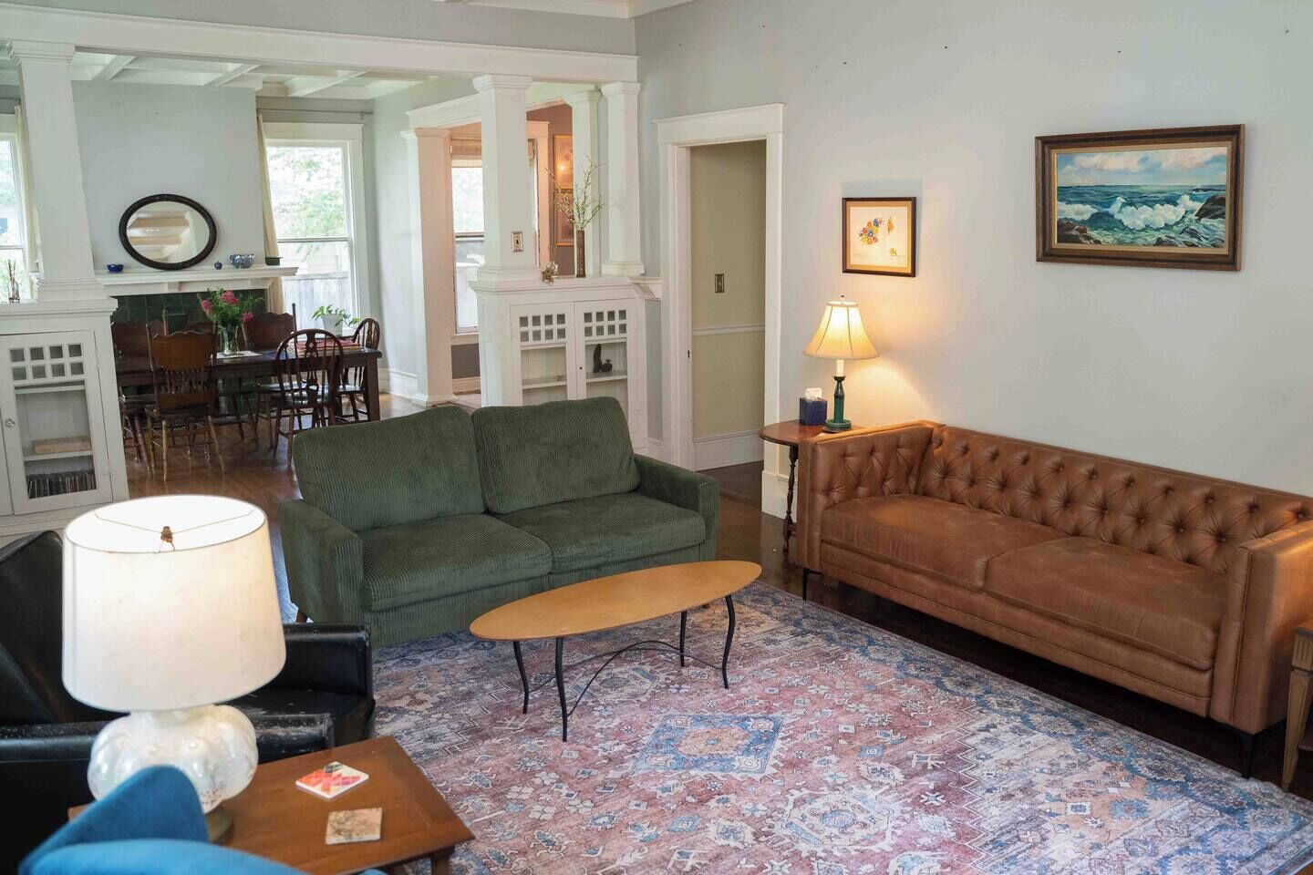 Un salon avec un canapé vert, un canapé marron, une table basse et une lampe. Un tapis à motifs recouvre le sol.