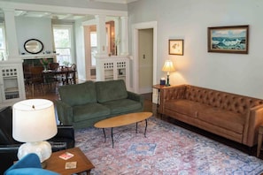 A living room with a green sofa, a brown sofa, a coffee table, and a lamp. There is a patterned rug on the floor. - Porch swing, 1920s home, walk to live music (Clarksdale)