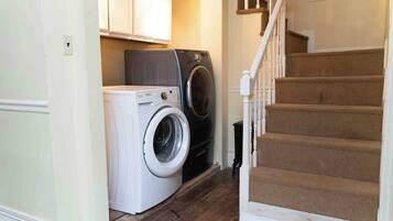A laundry area with a washing machine and dryer, a staircase with carpeted steps, and a white door.